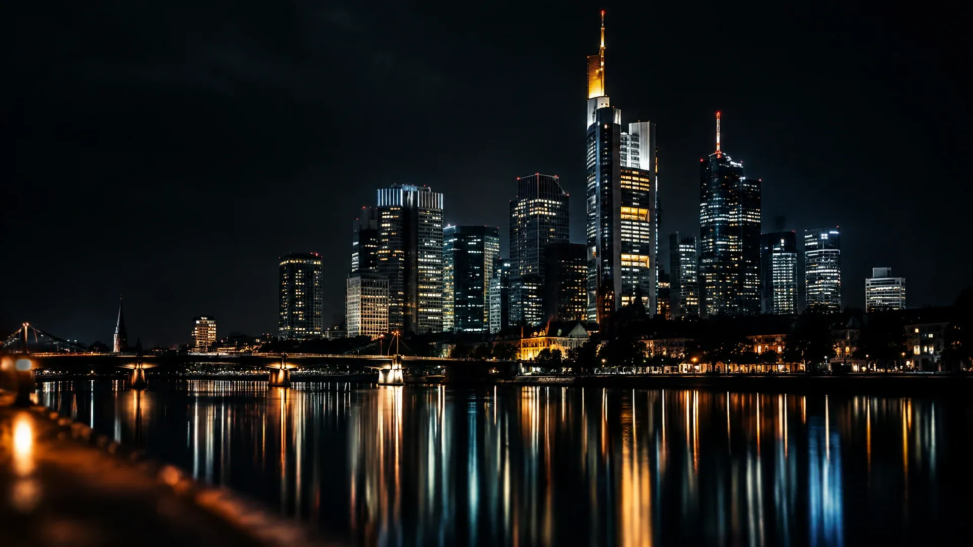 Night-time skyline of a banking district seen from the riverbank, the lights of the tower blocks reflected in the water