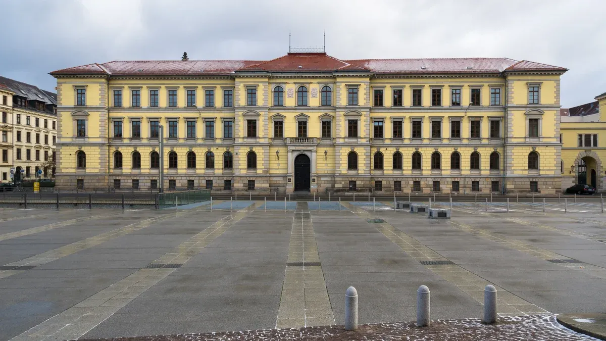 Gelbes Gerichtsgebäude des Landgerichts Leipzig mit rotem Dach hinter einem weiten gepflasterten Platz