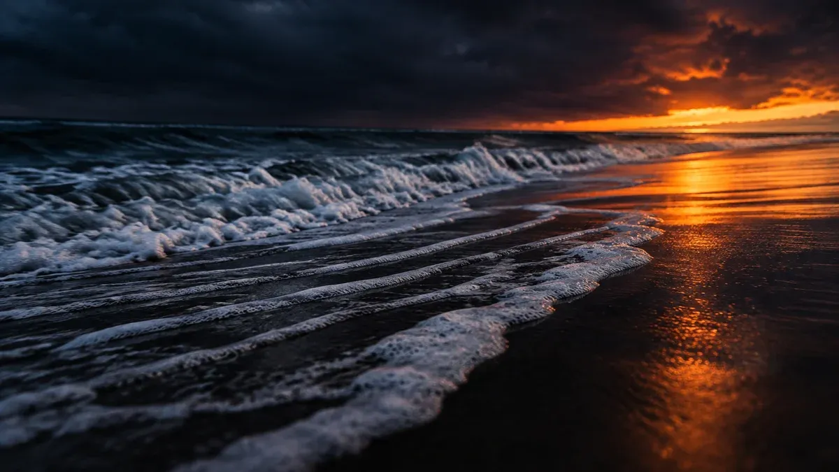 Brandung zieht sich bei Dämmerung über dunklen Sand ins Meer zurück
