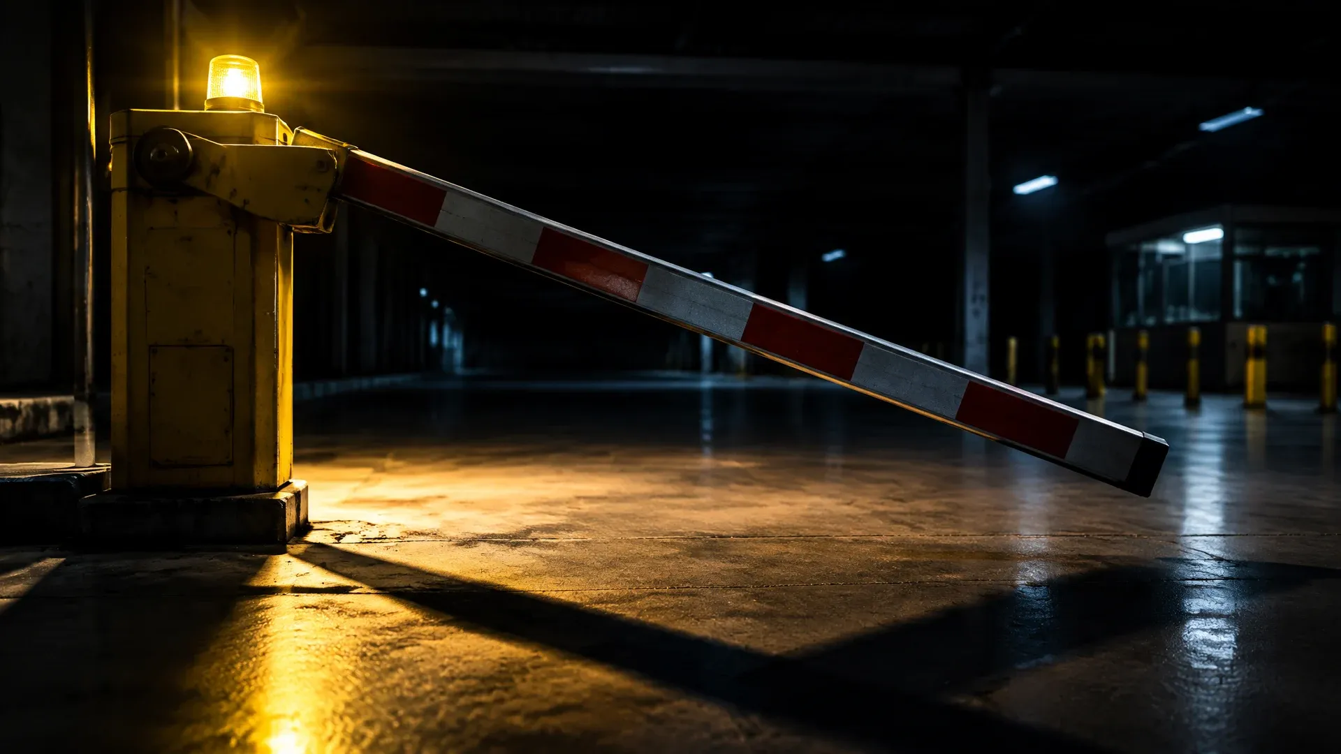Schlagbaumschranke senkt sich in einer leeren Abfertigungshalle bei Nacht, ein gelbes Rundumlicht wirft harte Schatten auf den Betonboden