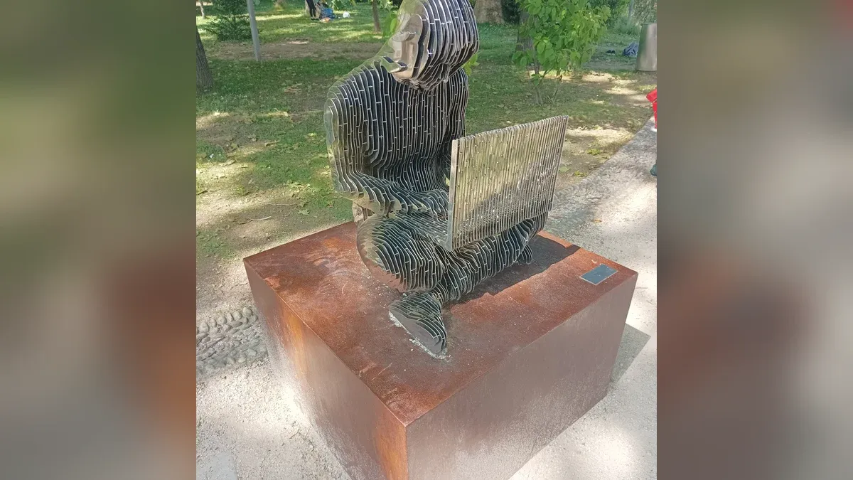 Metallskulptur einer sitzenden Figur mit Laptop aus senkrechten Stahllamellen auf einem rostroten Sockel in einem Park in Lugano