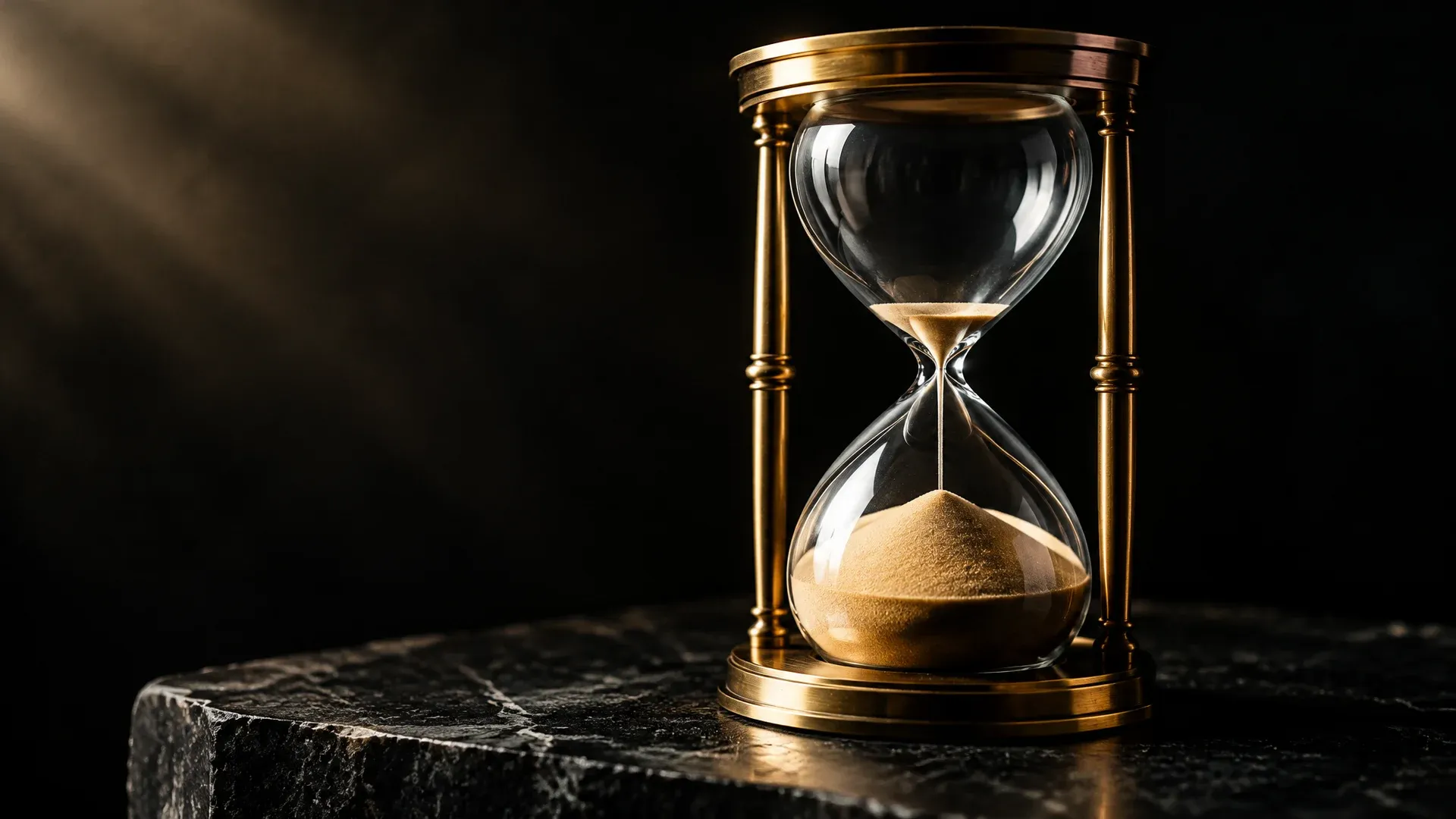 Messing-Sanduhr auf dunkler Steinplatte, im oberen Glas liegt nur noch eine duenne Schicht Sand