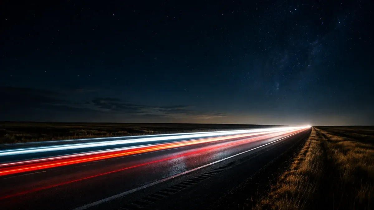 Light trails racing at night along a dark highway through flat prairie land