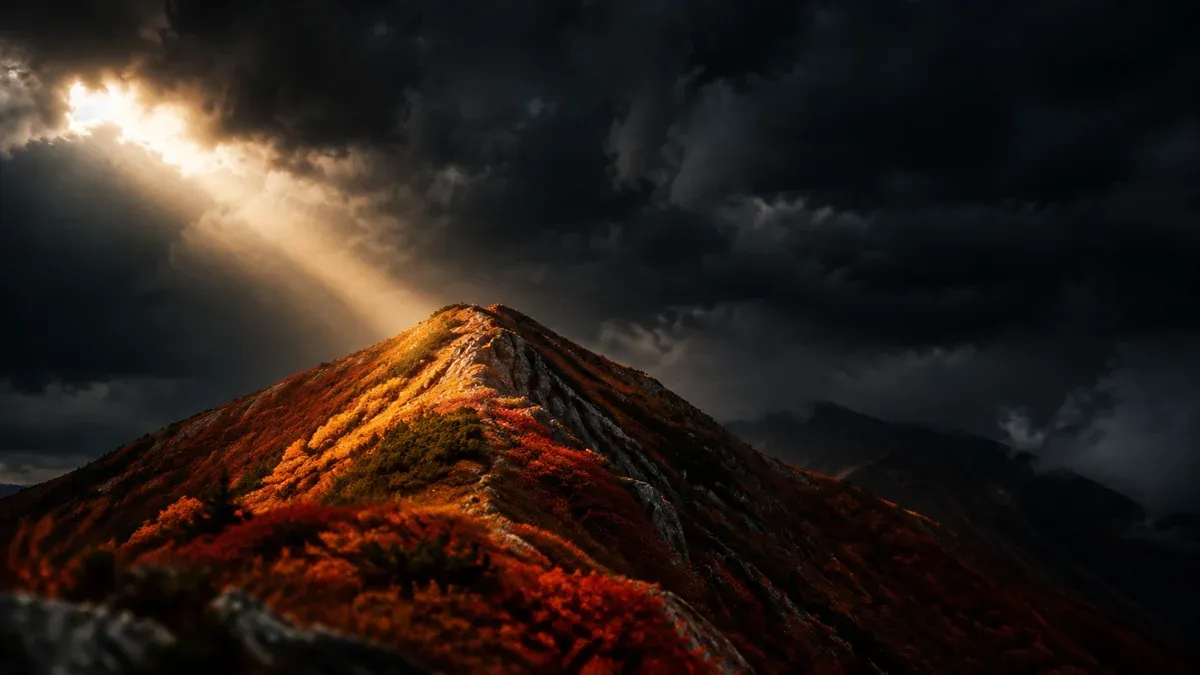 Black wall of cloud moving in over an autumn-red mountain ridge with a single shaft of sunlight from the side